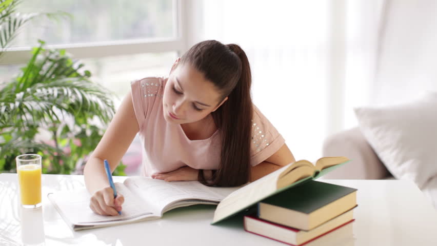 Cheerful student girl studying at table with books drinking juice and smiling