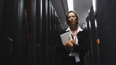 IT businesswoman inspects data center servers. Working in computer server room data center. Walking along rows of super computers, racks of airconditioned cpu's.