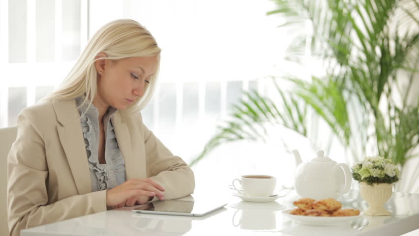 Pretty businesswoman sitting at table using touchpad and smiling at camera