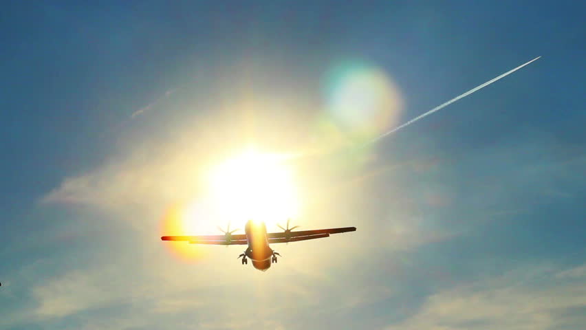 Airplane landing silhouette through sun rays, daytime, blue sky
