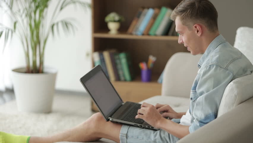 Young guy sitting on couch and using laptop