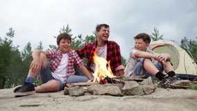 Cheerful dad and his kids having a good time sitting by the fire