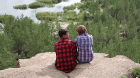 Dating couple sitting on the cliff with breathtaking view right in front of them