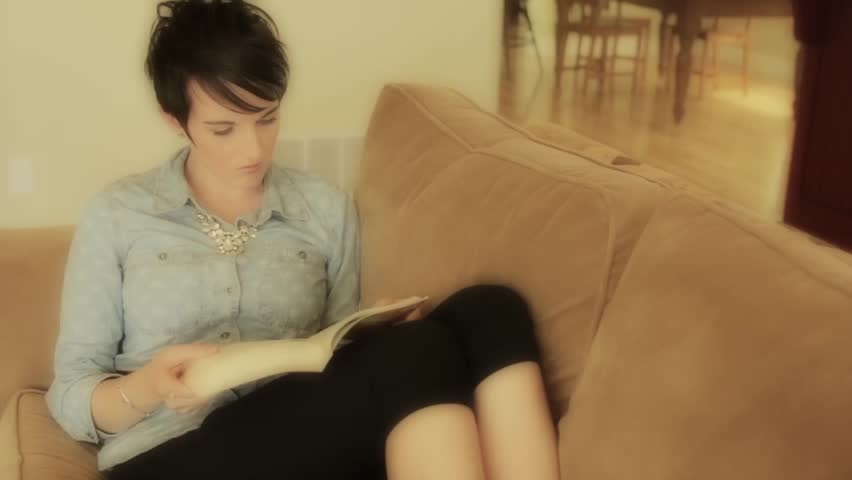 A woman resting on her couch while reading a book in her house
