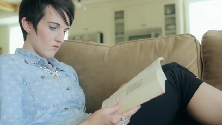 A woman relaxing and reading a book on a comfortable couch in her home