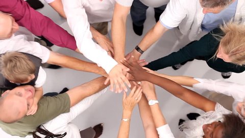 Group of people coming together and joining hands to form a happy close group of individuals. Shot from above in large white studio. High quality HD video footage