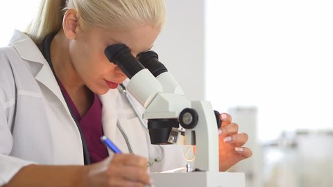 Medical researcher using microscope and writing notes