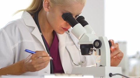 Medical researcher using microscope and writing notes
