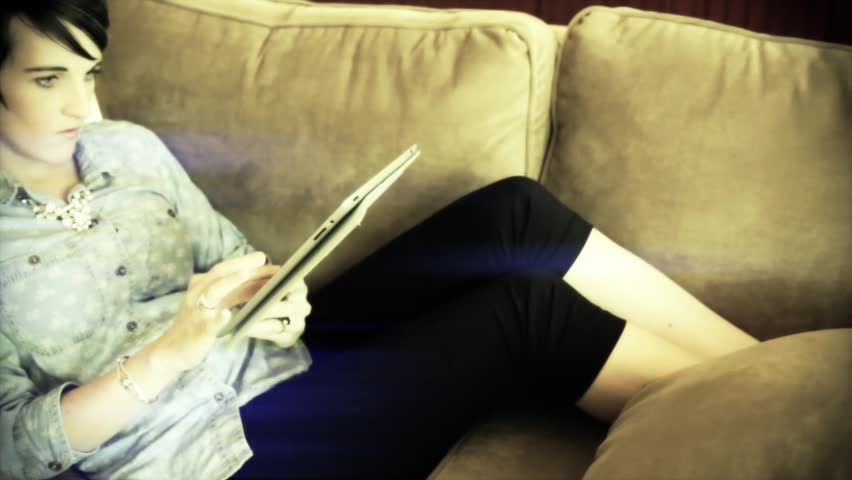 A woman shopping on a tablet for wedding dresses while relaxing on a couch in
