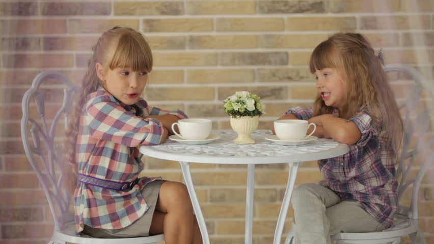 Two little girls sitting at table at cafe and talking over cup of tea