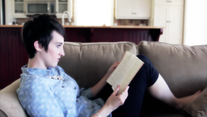 A woman sitting comfortably on her couch while reading a book.