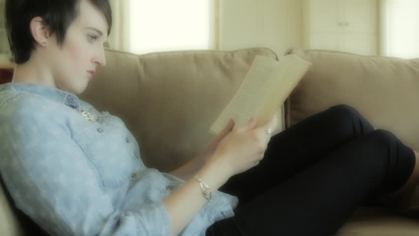 A woman sitting comfortably on her couch while reading a book.