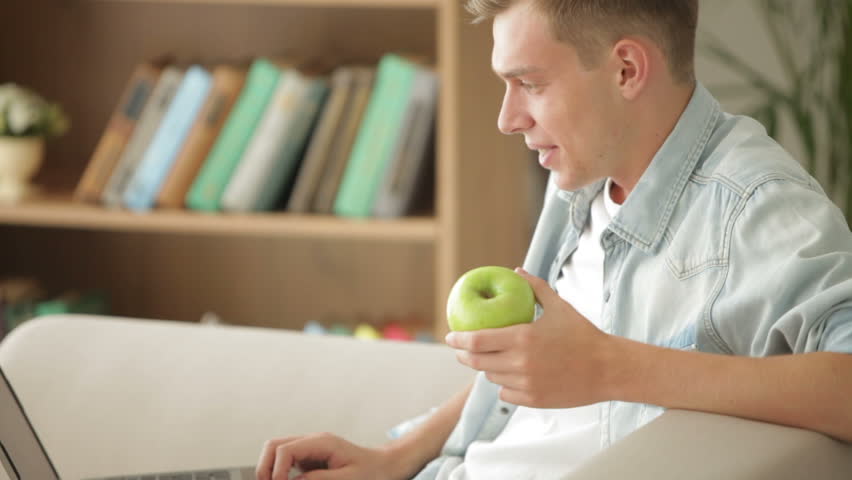 Handsome man using laptop and eating apple