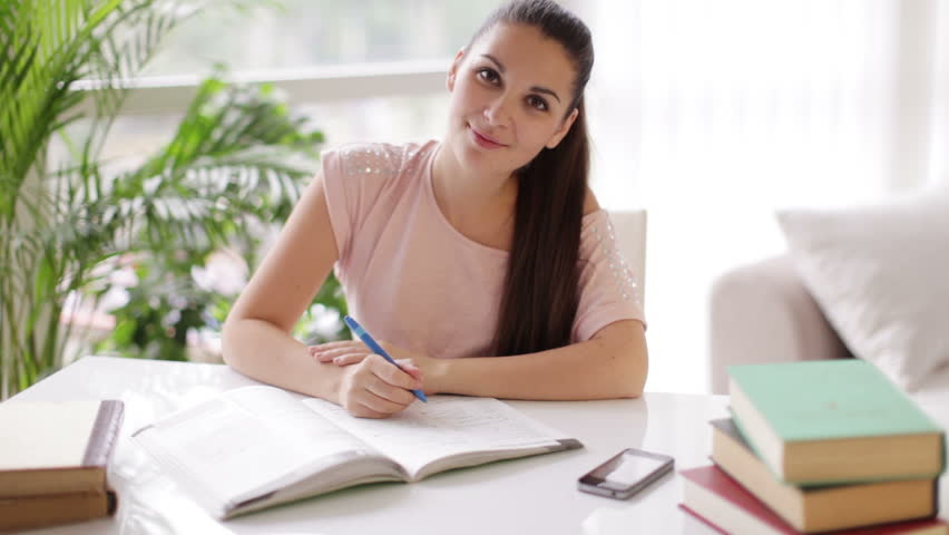 Attractive girl studying at table with books and looking at camera with smile