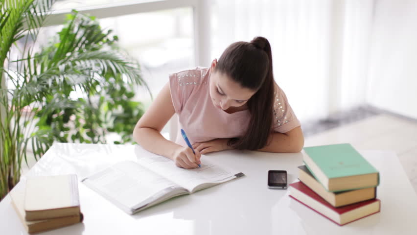 Attractive girl sitting at table studying with books and writing in notebook