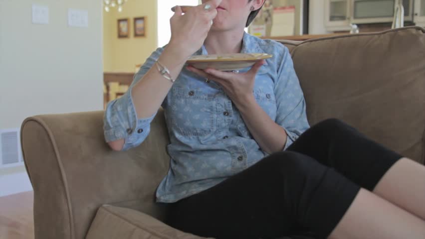 A woman eats while relaxing on the couch in her home