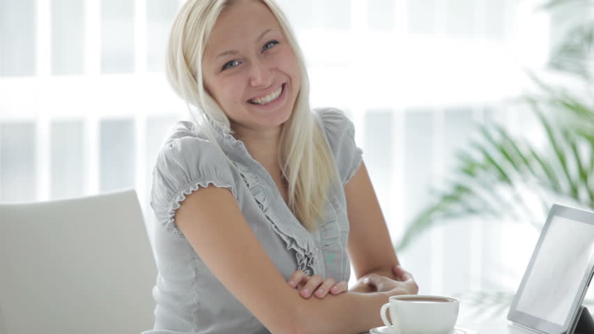 Attractive young woman sitting at table with cup of tea and using touchpad