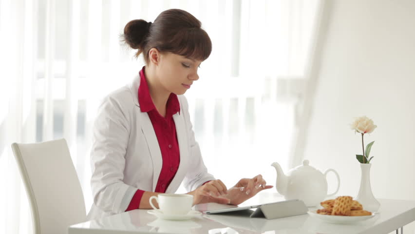 Beautiful young woman sitting at table with cup of tea and using tablet