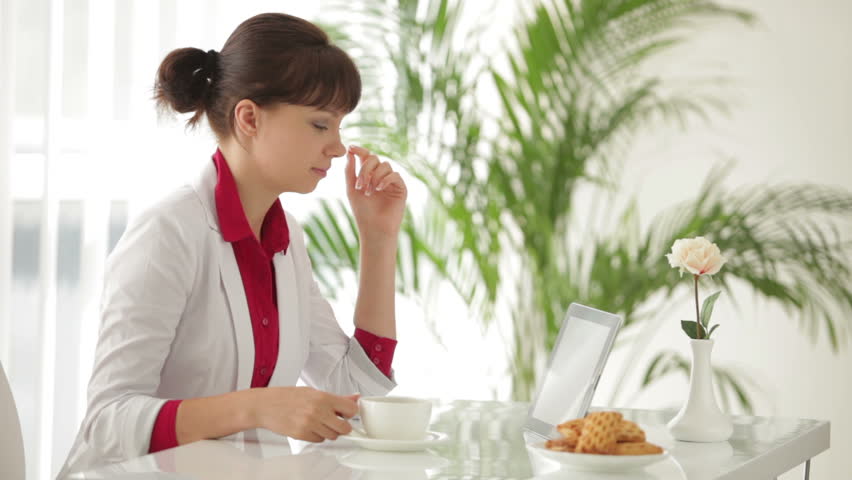 Charming girl sitting at table drinking tea and using tablet