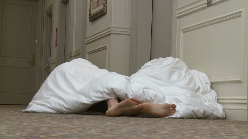 Couple resort to sleeping in hotel corridor. Feet appear under the blanket.