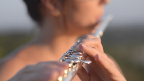 Female musician plays flute outdoors. Detail view of fingers