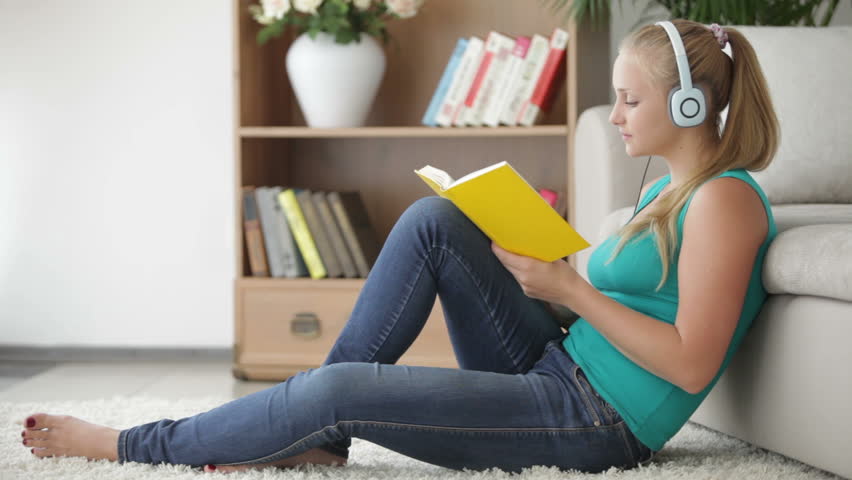 Charming girl reading book and listening music with smile