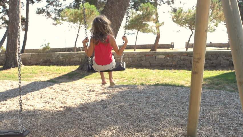Slow Motion Shot Of A Girl Jumping Off A Swing In Park. Shot In Her Back. 