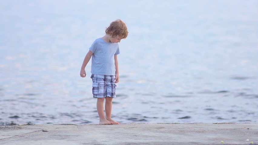 Slow Motion Shot Of A Cute Little Boy By The Seaside. Walks Towards Camera And