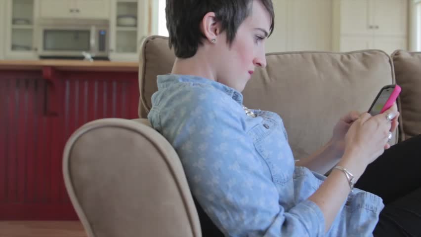 A woman sending a text message from her smart phone while resting on the couch