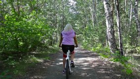 Rear view of a woman cycling through the summer forest