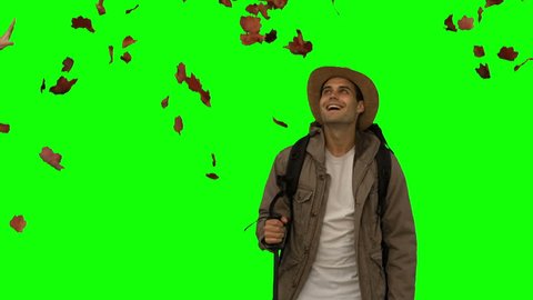 Cheerful man standing under leaves falling on green screen in slow motion
