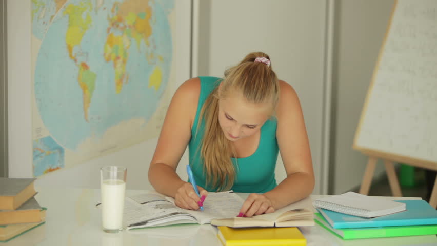 Beautiful student sitting at table with notebook and drinking milk