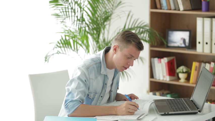 Attractive man sitting at table using laptop and writing in notebook