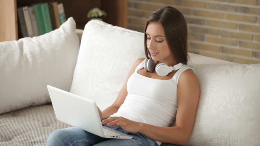 Young woman sitting on sofa using laptop closing it and smiling