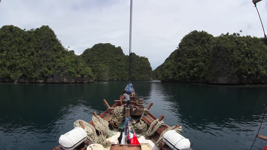 An Indonesian pinisi schooner sails toward a set of limestone islands in Raja
