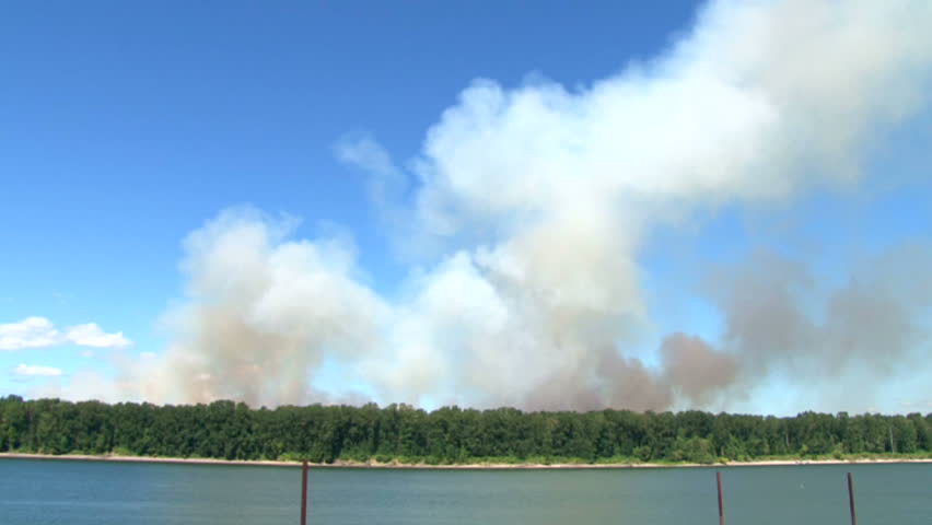 Forest fire burns wild on Government Island in Oregon on windy, sunny day.