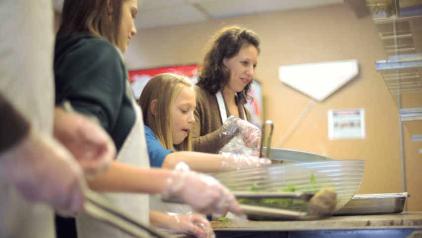 A young family works at a soup kitchen helping the homeless by serving them hot food