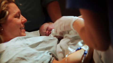 Woman gives birth. Witness the actual moment of when the baby girl is cleaned, tended by nurses and then greets her exhausted but exuberant mother. The mother's face is full of joy, relief and delight