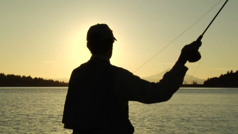 Stunning sunset shot of a fly-fishermen fishing a mountain lake.  Silhouette.
