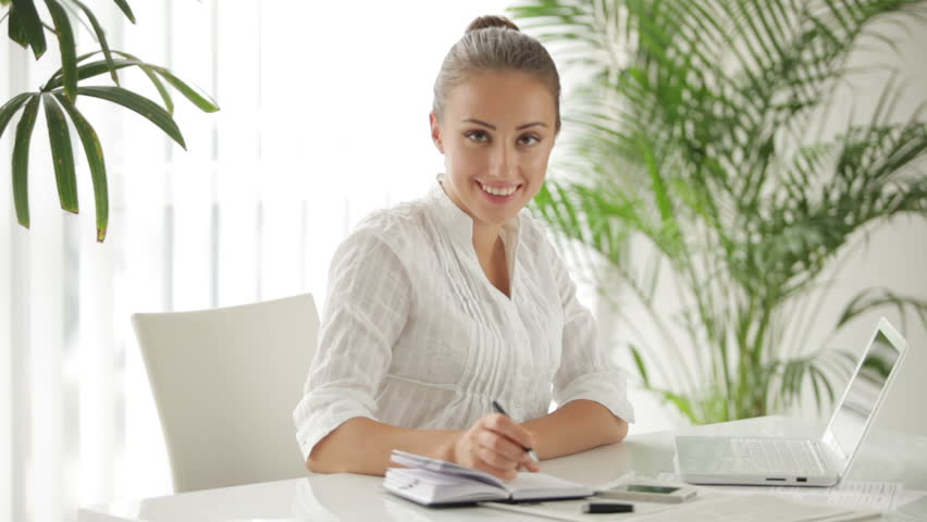 Attractive woman sitting at table using laptop and writing in notebook