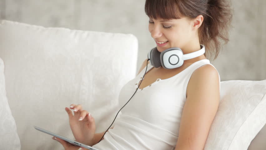 Beautiful girl in headset sitting on sofa and using touchpad