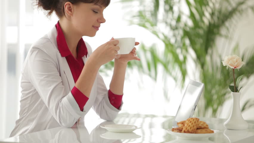 Attractive girl sitting at table drinking tea and using tablet