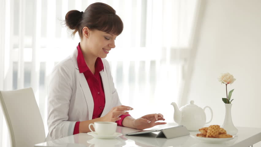 Beautiful young woman sitting at table drinking tea and using tablet