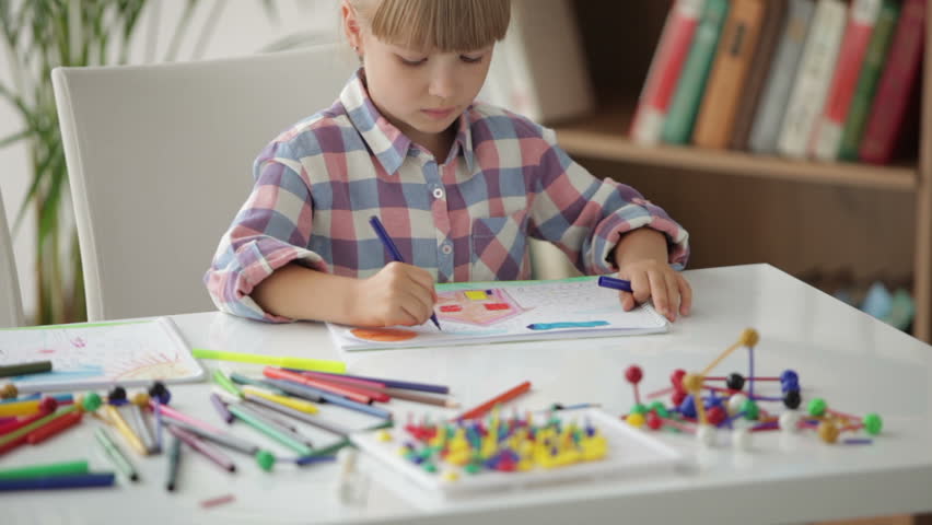 Beautiful little girl sitting at desk drawing with colored pencils and smiling