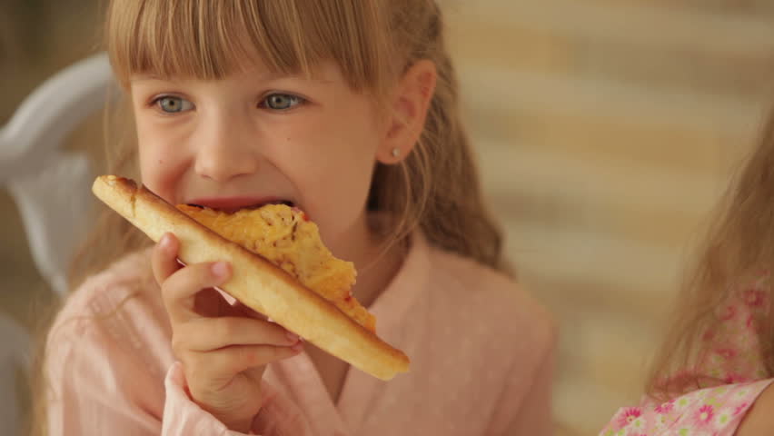 Two funny little girls eating pizza and smiling at camera