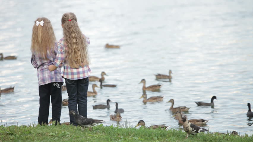 Two cute little girls at park feeding ducks