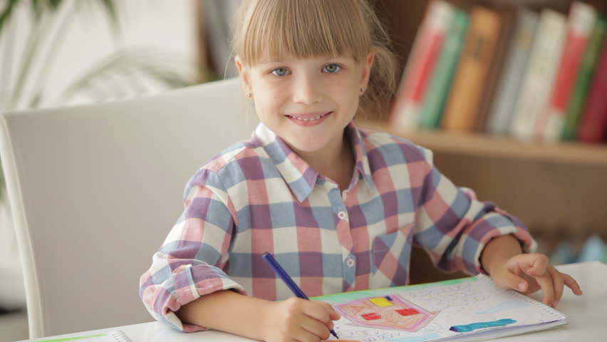 Funny little girl drawing with colored pencils and smiling at camera