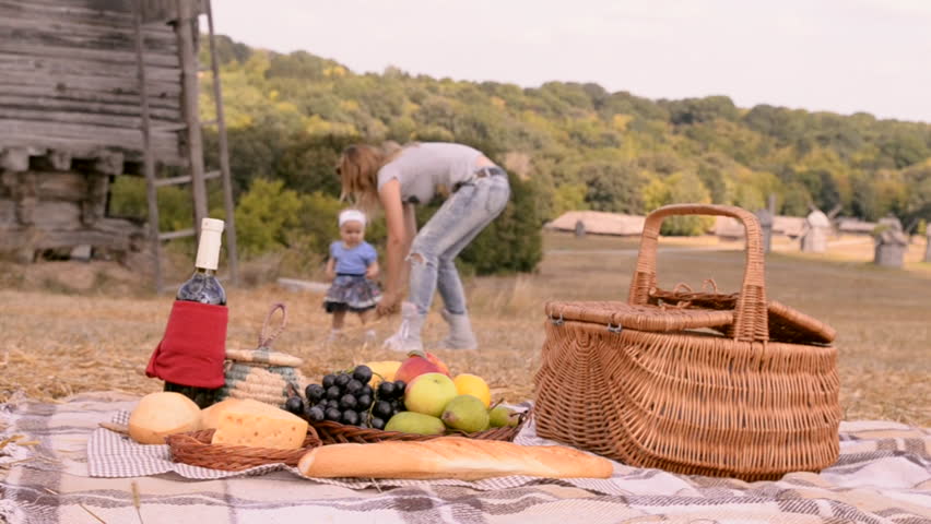 mother and daughter throwing straw in the background on the countryside picnic, the windmill on the background, fruit and straw basket in the front