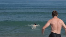 Young exited man jumping to the sea having fun with his girlfriend