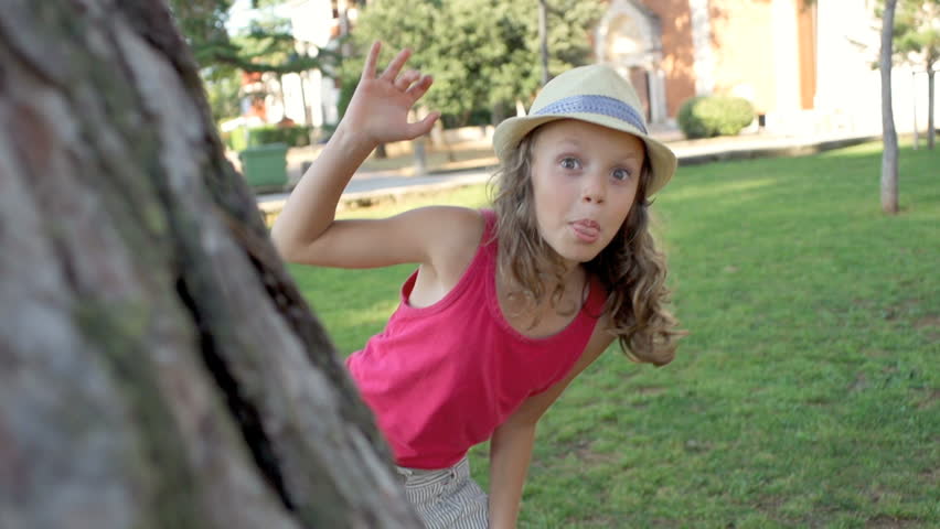 Slow Motion Shot Of A Cute Girl Peeking From Behind A Pine Tree And Making Funny